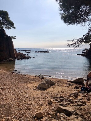 Una spiaggia rocciosa con acque cristalline e imbarcazioni all'orizzonte.