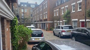 Una estrecha calle empedrada de ladrillo con coches aparcados y casas escalonadas.