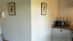 Ein kleiner, sauberer Raum mit einer Küchenzeile, einem grauen Sessel und zwei gerahmten Bildern an der Wand.