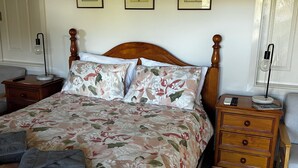 Ein ordentlich bezogenes Bett mit Blumenmuster, ein hölzernes Kopfteil und ein Nachttisch mit Lampe und Telefon.
