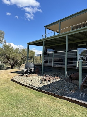 A modern building with a covered patio area, a barbecue grill, and a landscaped garden with rocks and grass.
