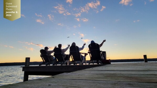 Four people sitting on a wooden dock facing a body of water at sunset.