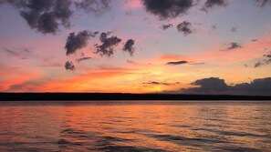 A sunset over a calm body of water with a silhouette of land in the distance.