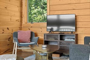 A cozy room with a wooden interior, a flat-screen TV mounted on the wall, a grey armchair with a patterned pillow, and a small round table. - Hygge on Seneca: "Relaxing Seneca Lake Getaway!" (Lodi)
