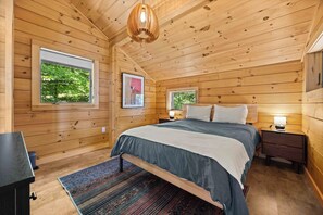 A wooden cabin bedroom with a bed, bedside tables, a rug, and a hanging light fixture. - Hygge on Seneca: "Relaxing Seneca Lake Getaway!" (Lodi)