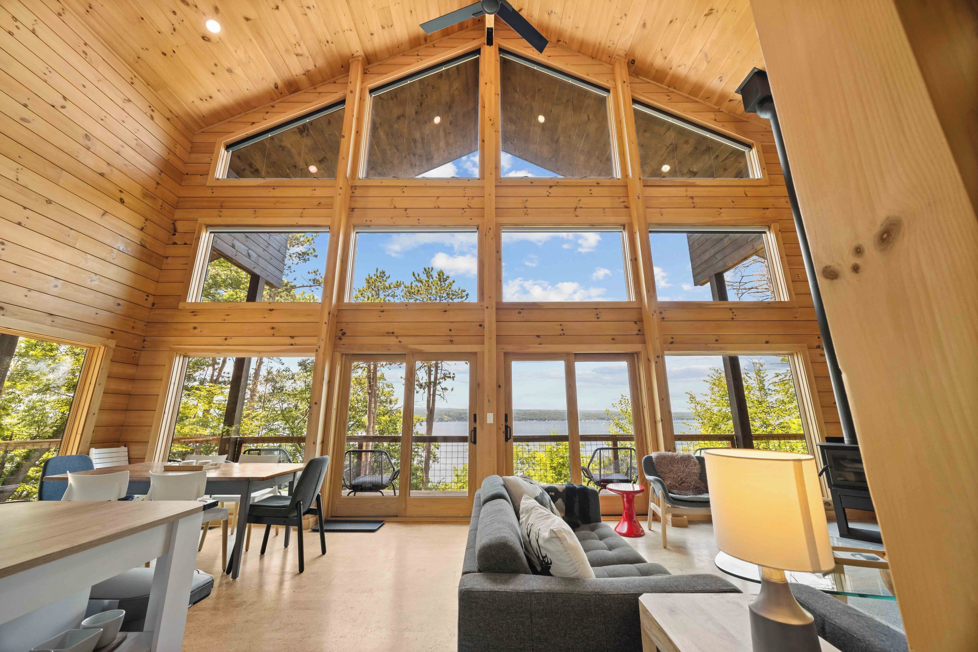 A spacious room with a high ceiling and large windows offering a view of trees and a body of water.