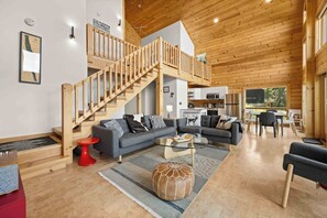 A spacious living area with a wooden staircase, two sofas, a glass coffee table, and a kitchen in the background. - Hygge on Seneca: "Relaxing Seneca Lake Getaway!" (Lodi)