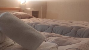 Habitación de hotel con dos camas, cada una con un edredón blanco y almohadas. Hay una mesita de noche con una lámpara y una pequeña mesa.