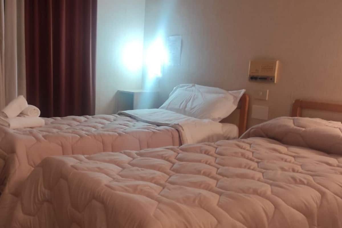 A hotel room with two beds, each with a pink quilted bedspread and white pillows. There is a nightstand with a lamp between the beds.