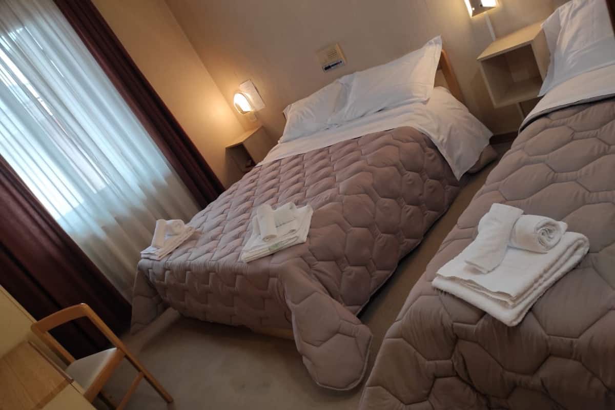 A hotel room with two beds, each with a brown quilted bedspread and white pillows. There are towels neatly folded on each bed.