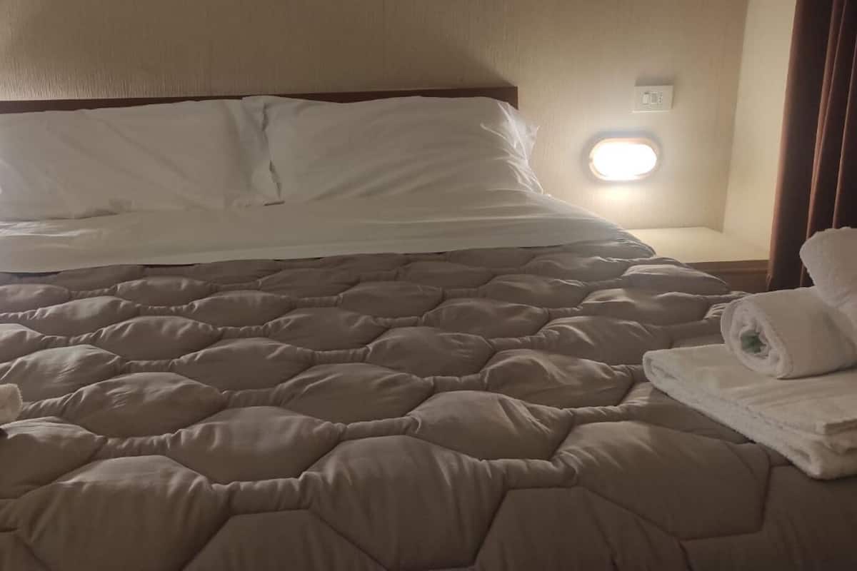 A neatly made bed with a quilted cover, a white pillow, and a rolled towel on the side.