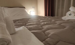A neatly made bed with a white comforter and pillows, a bedside lamp, and a rolled towel on the right side. - Hotel Centrale (Chiusi)