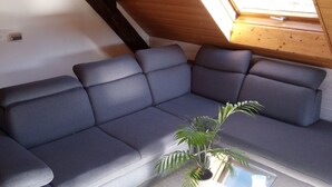 Une chambre de style loft moderne, dotée d’un grand canapé d’angle, d’une lucarne et d’une plante en pot.