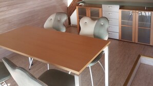 Un coin repas avec une table et des chaises en bois, une cuisine équipée de placards et un plafond en pente avec des poutres apparentes.