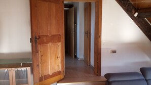 Une pièce avec un plafond en bois, une grande porte ouverte donnant sur un couloir, un canapé et une petite table.