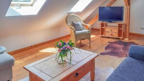Un dormitorio estilo loft acogedor, con suelo de madera, una silla de mimbre, un televisor sobre un mueble de madera y un florero en una mesa de centro.