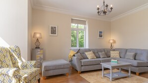 A living room with a grey sofa, a patterned armchair, a small table, and a chandelier. - Relaxing Private Country Escape with Hot Tub (Castlerea)