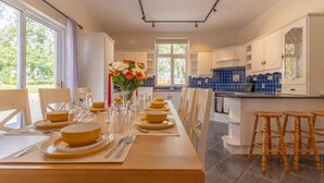A modern kitchen with a dining area set for a meal, featuring a long table, chairs, and a vase of flowers. - Relaxing Private Country Escape with Hot Tub (Castlerea)