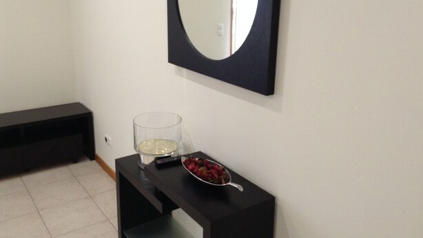Une pièce avec une console noire, un vase en verre rempli de fleurs, une télécommande et un miroir accroché au mur.