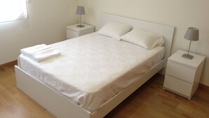 Un lit bien fait, avec du linge de lit blanc et des oreillers, deux tables de chevet avec des lampes et une fenêtre sur le côté gauche.