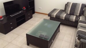 Un salon doté d’un téléviseur à écran plat, d’une table basse en verre, d’un canapé à rayures et d’un meuble de rangement noir pour les appareils multimédias.
