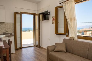 Ein Wohnzimmer mit einer Couch, einem an der Wand befestigten Fernseher und Meerblick durch eine Glastür.