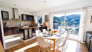 Une cuisine moderne avec des meubles de couleur sombre, un îlot central et un coin repas avec des chaises blanches et une table mise pour le petit-déjeuner.