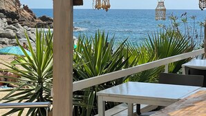 Une terrasse au bord de la plage, agrémentée de coquillages décoratifs suspendus, et offrant une vue sur l’océan.