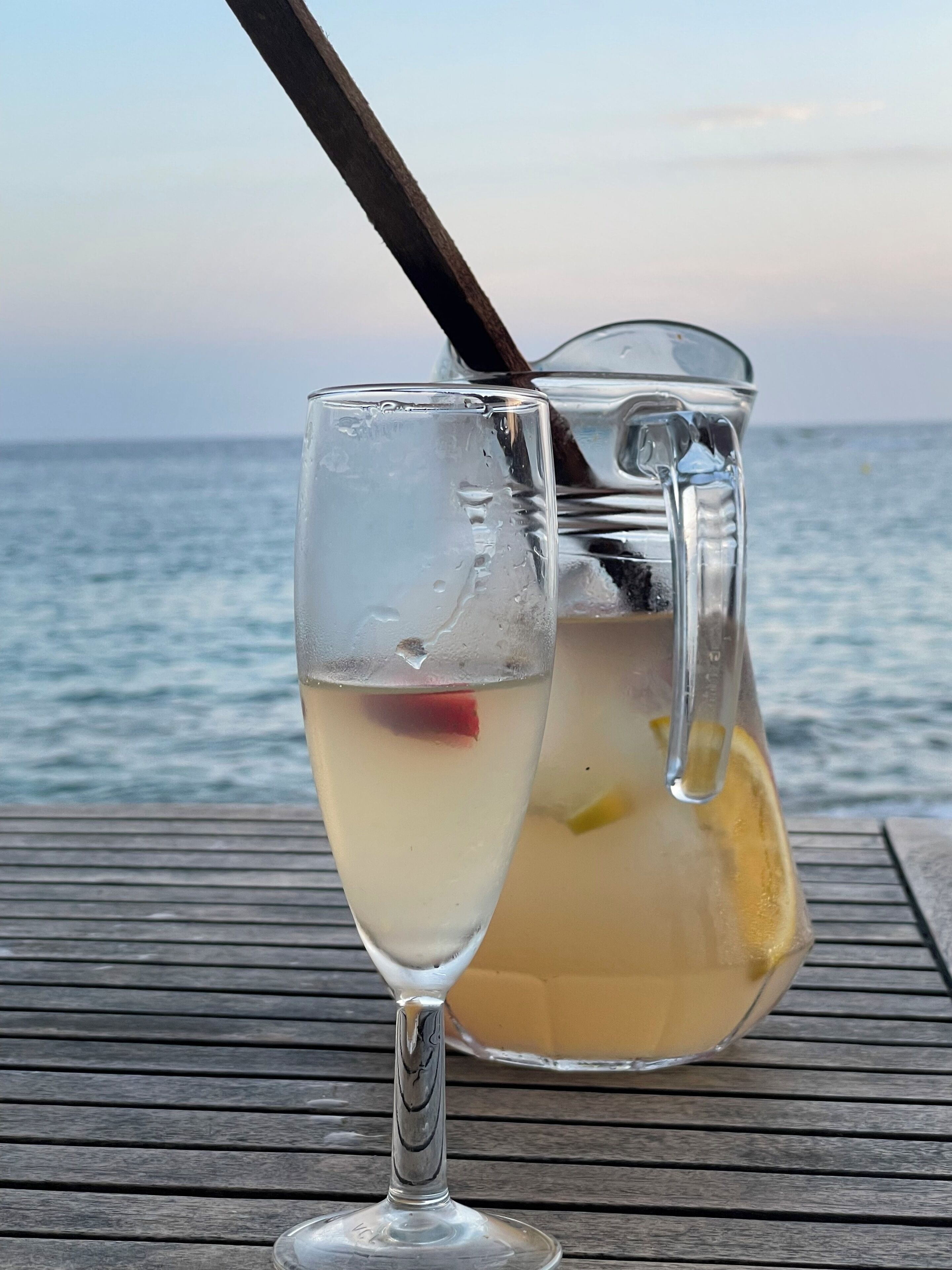 Ein Glas mit einem weißen Getränk und einem Strohhalm auf einem Holztisch am Meer.