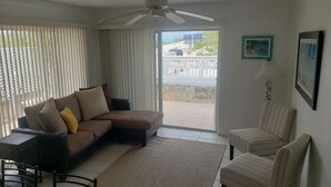 A living room with a sofa, two armchairs, a ceiling fan, a view through a glass door to an outdoor area, and a small table with chairs. - Beach Front Villa (Abaco)