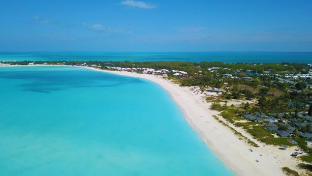 An aerial view of a beach with clear turquoise waters, a sandy shore, and a resort area with buildings and greenery. - Beach Front Villa (Abaco)
