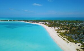 Vista aérea de uma praia com águas turquesa cristalinas, areal arenoso e área de resort com edifícios e vegetação.