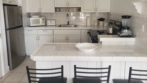 A kitchen with white cabinets, a stainless steel refrigerator, a microwave, a toaster, a sink, a blender, and a bowl on the island. - Beach Front Villa (Abaco)