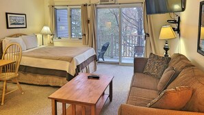 Una habitación de hotel con cama, sofá, mesa, televisor y balcón con sillas.