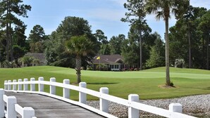 Un parcours de golf avec un pont en bois blanc menant à un club-house.