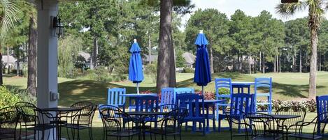 Un espace extérieur abrité, avec des tables et des chaises bleues, des parasols et une vue sur un terrain de golf.
