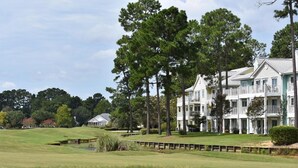 Un grande edificio a più piani con balconi, immerso in un campo da golf con uno stagno e alberi.