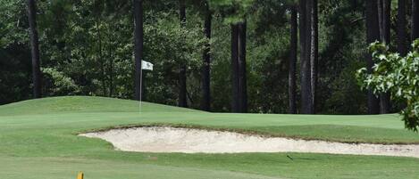 Un parcours de golf avec un bunker de sable et un drapeau indiquant le trou.