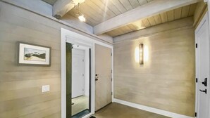 Un couloir avec un plancher en bois, un tableau encadré au mur, une porte avec un miroir et un luminaire.