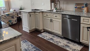 A modern kitchen with white cabinetry, granite countertops, and a stainless steel dishwasher. - Summer Fling 2nd Floor Downtown Suite  (South Haven)