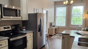 A modern kitchen with stainless steel appliances, wooden cabinets, and a large island with a sink. - Summer Fling 2nd Floor Downtown Suite  (South Haven)