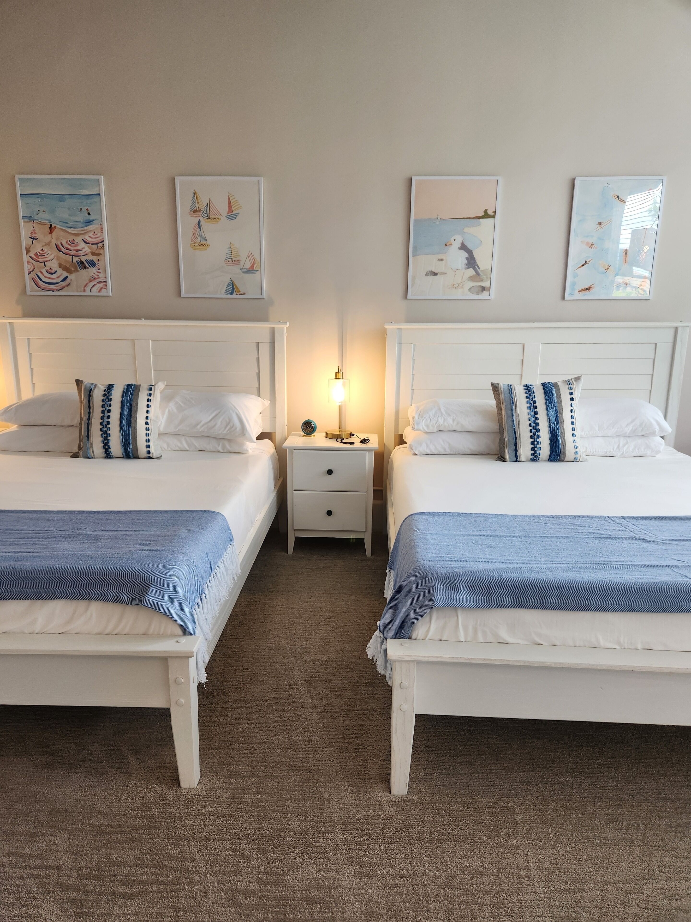Een hotelkamer met twee bedden, witte hoofdeinden en kunstwerken aan de muur.
