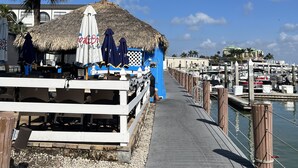 Une jetée surmontée d’une structure à toit de chaume, avec une clôture en bois, d’où l’on peut admirer le port de plaisance et les bateaux.
