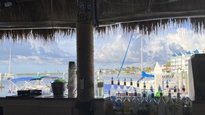 Un espace bar offrant une vue sur un port de plaisance et sur des bâtiments en arrière-plan.