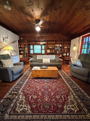 A cozy living room with a wooden ceiling, a central sofa, a coffee table, and a patterned rug.