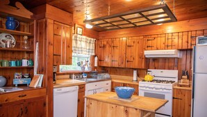 A wooden cabin-style kitchen with a central island, white appliances, and wooden cabinets. - Adirondack Retreat - Hot Tub & Lake (Keeseville)