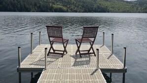 A wooden dock with two chairs facing a calm lake, surrounded by a forested hillside. - Adirondack Retreat - Hot Tub & Lake (Keeseville)