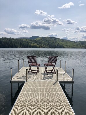 A wooden dock with two chairs facing a calm lake, surrounded by a forested hillside.