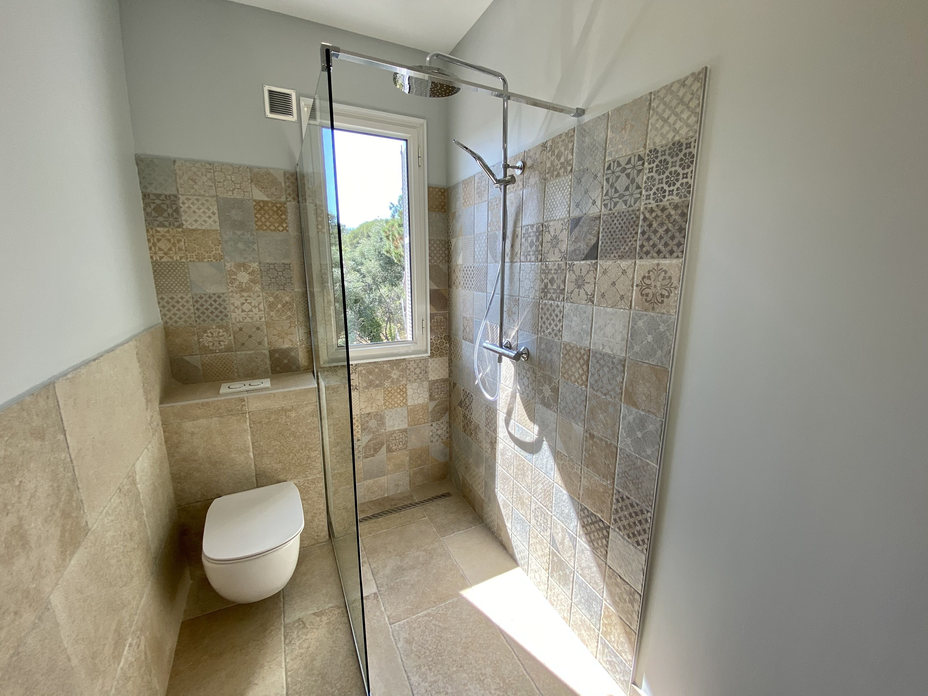 Une salle de bain moderne avec une douche à parois de verre, des toilettes et des carreaux à motifs.