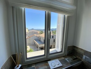 A room with a large window offering a view of buildings and mountains.